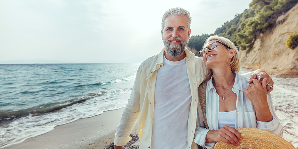 Senior couple walking peacefully on a sunny beach, smiling and relaxed during their trip.